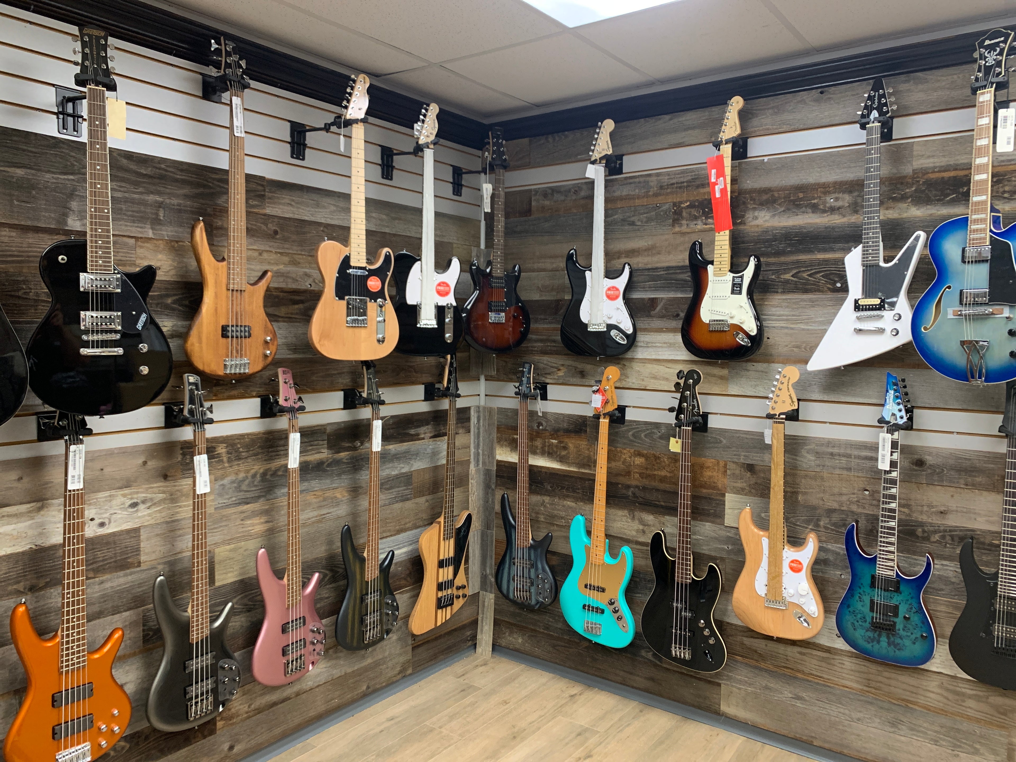 Showroom Wall with wooden background with a mix of 20 electric guitars and basses